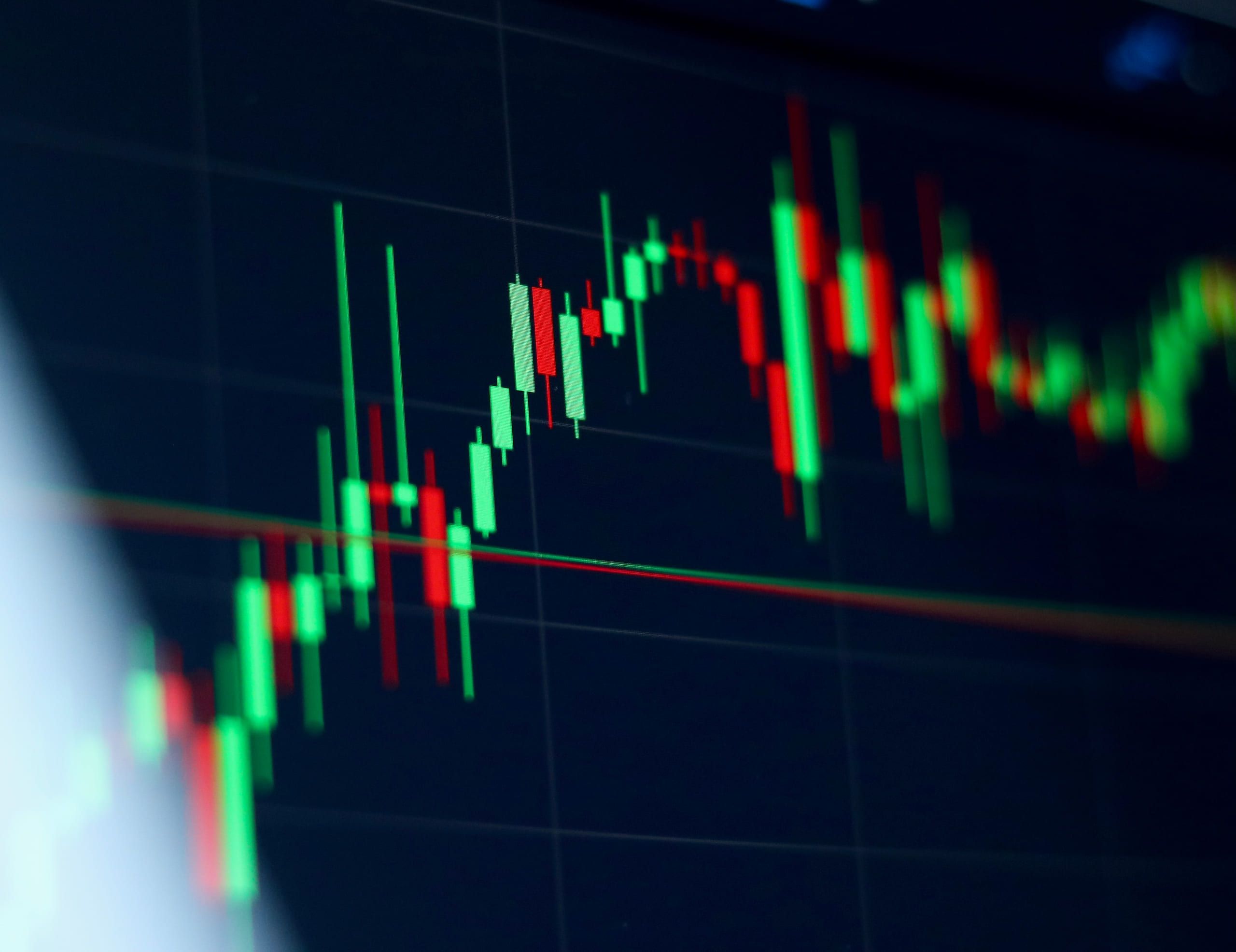 A close, shallow-focus photograph of green and red candlesticks on a dark trading screen.